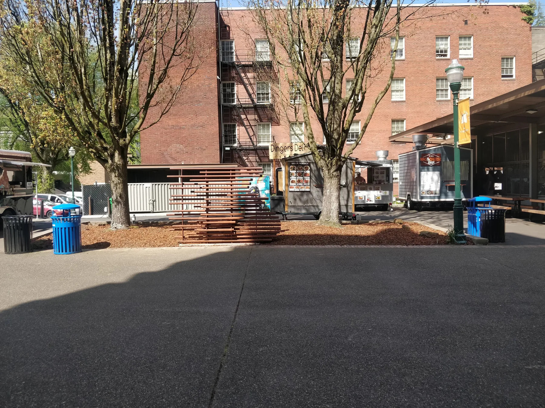 The sculpture in place under the trees, with food carts and a brick building behind