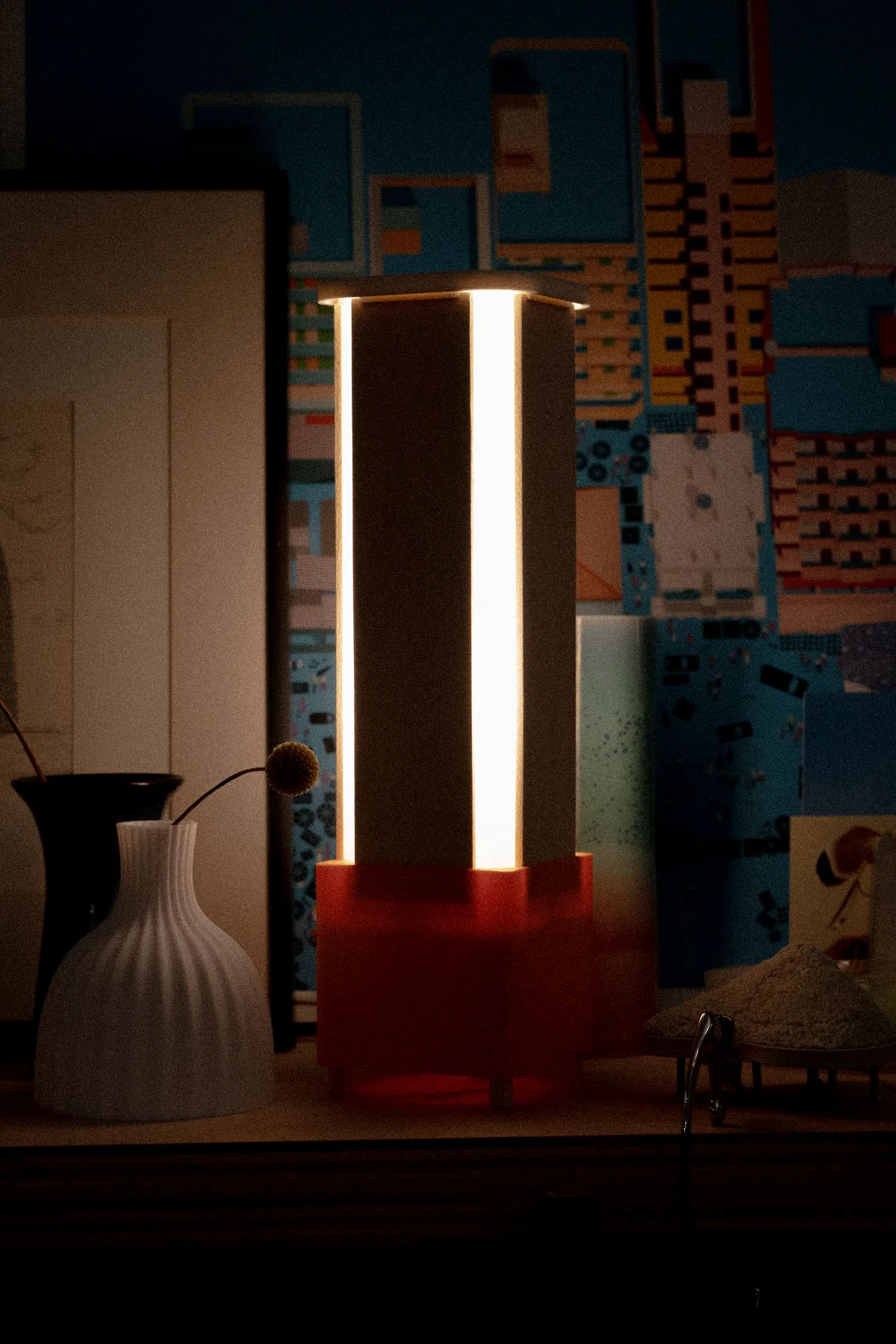 The lamp lit on a shelf, a column of warm light on a red base