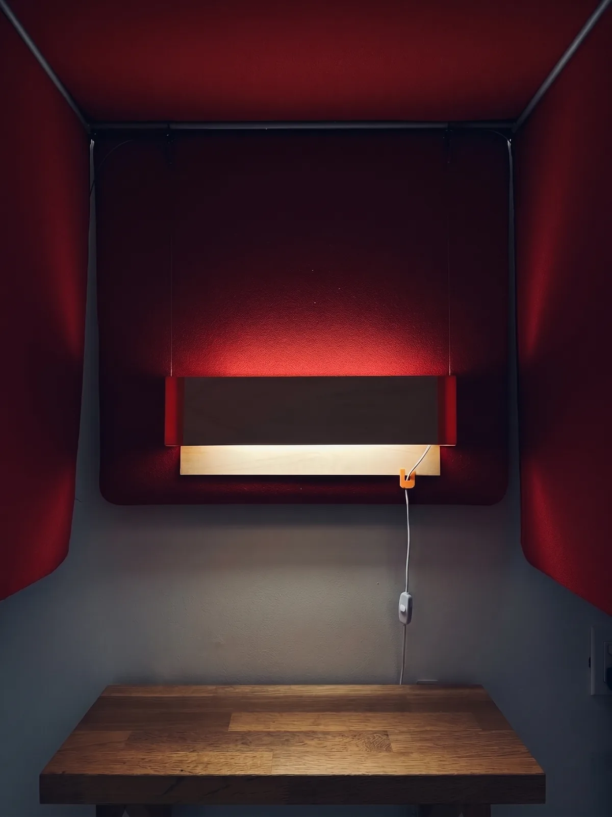 The sconce lit at night over a desk in a red felt alcove